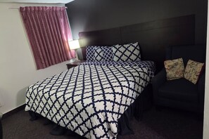 Ein Hotelzimmer mit einem Bett, einem Nachttisch, einer Lampe und einem dunkel gefärbten Sessel.