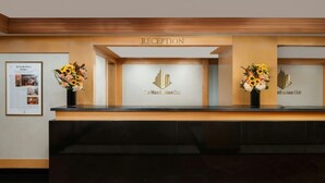 En receptionsdisk med en skylt som visar texten ”RECEPTION” och logotypen för ”The Manhattan Club”. På vardera sidan av disken står det två vaser med blommor.