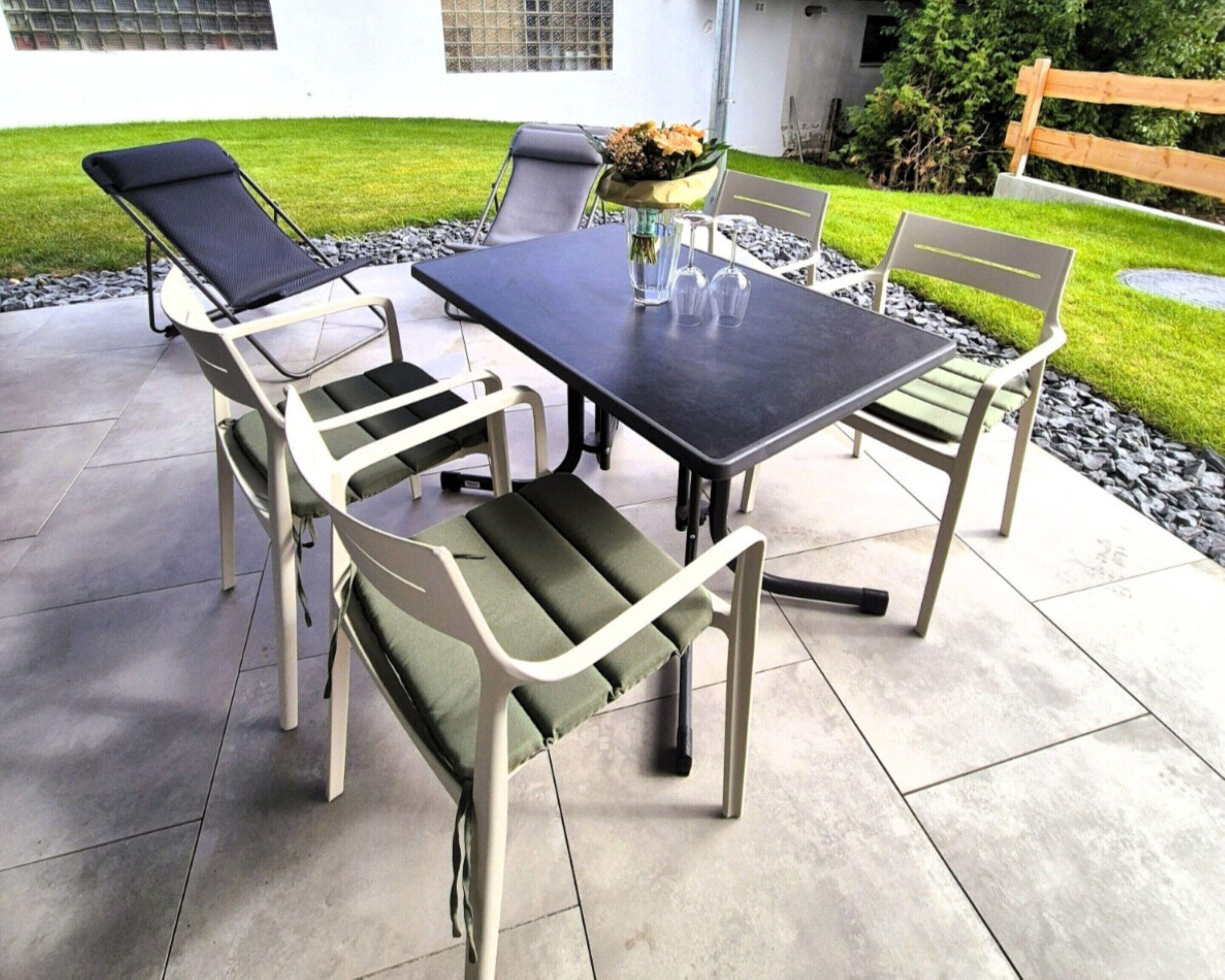 Une terrasse extérieure avec une table et des chaises, un vase rempli de fleurs et, au fond, une clôture en bois.
