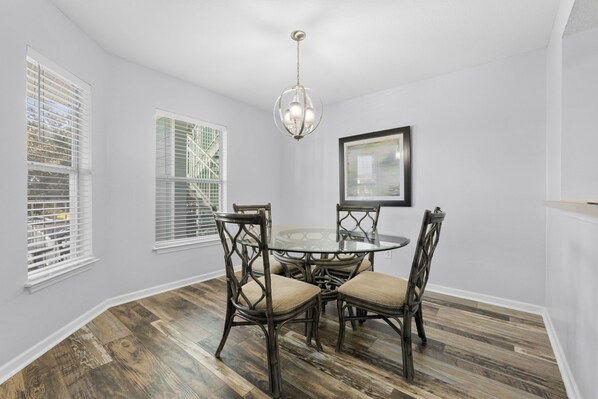 A dining area with a round glass table surrounded by four chairs with cushioned seats.