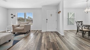 Un salon spacieux avec un canapé beige, un pouf à rayures et un coin repas comprenant une chaise et une table en bois.