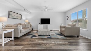 Un salon moderne avec un canapé, un pouf et un téléviseur à écran plat posé sur un meuble.