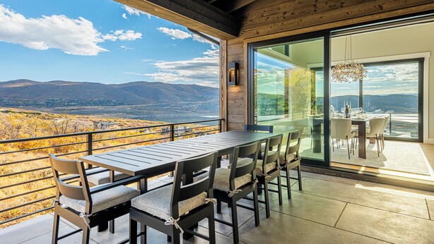 A dining area with a table and chairs, a large window with a view of mountains, and a chandelier. - Five-Star Base for Powder Runs & Lake Days - Adventure Elevated (Heber City)