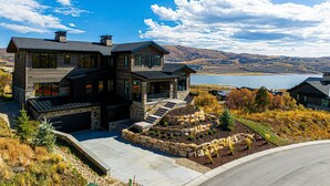 A large, modern two-story house with a stone facade, a garage, and a landscaped front yard with a stone retaining wall and steps leading to the entrance. - Five-Star Base for Powder Runs & Lake Days - Adventure Elevated (Heber City)