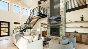 A spacious living area with a staircase, a fireplace, and a view of the outdoors. - Five-Star Base for Powder Runs & Lake Days - Adventure Elevated (Heber City)