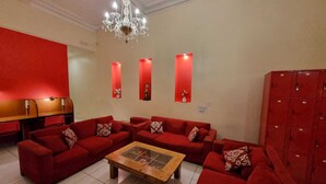 Un hall d’entrée spacieux avec des canapés rouges, une table basse en bois, un lustre et des casiers rouges.