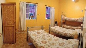Une chambre de dortoir avec des lits superposés, une armoire en bois et deux fenêtres avec des rideaux.