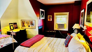 A bedroom with a bed, a desk, and a chair. There are pictures on the wall and a window with blinds. - The Burnt Toast Inn- Attic Suite (Ann Arbor)