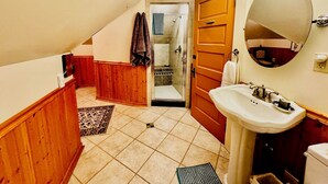 A bathroom with a sink, mirror, and wooden door. - The Burnt Toast Inn- Attic Suite (Ann Arbor)