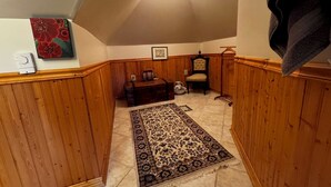 A cozy attic room with wooden paneling, a patterned rug, a chest of drawers, a chair, and a hanging light fixture. - The Burnt Toast Inn- Attic Suite (Ann Arbor)