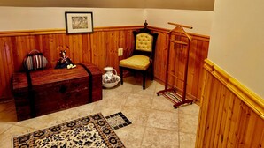 A corner room with wooden paneling, a bench, a chair, a small table, a decorative jug, and a hanging rack. - The Burnt Toast Inn- Attic Suite (Ann Arbor)
