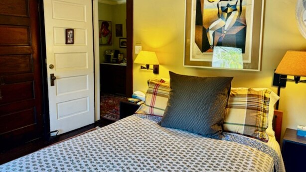A bedroom with a bed, a door, a painting, and a lamp. - The Burnt Toast Inn- Gold Room (Ann Arbor)