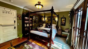 Un letto a baldacchino con copriletto, una libreria, uno specchio e una porta con attaccapanni.
