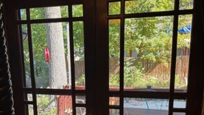 Una porta di legno con un motivo a griglia, che dà accesso a un'area esterna con un pavimento in legno, un albero e un'altalena blu.