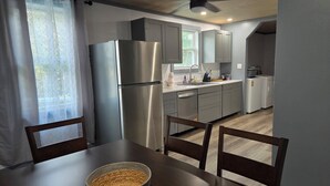 A modern kitchen with stainless steel appliances, grey cabinets, and a dining area with a wooden table and chairs.