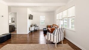 A spacious living room with a brown leather sofa, striped armchairs, and a television mounted on the wall. - Cozy Charming 2BR Cottage - Perfect for Traveling Professionals (Grosse Ile)