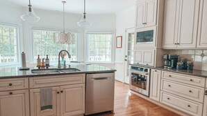 A kitchen with white cabinetry, a dishwasher, and a large window. - Putting Green - Life Sized Chess -Luxury Aesthetic (Greensboro)