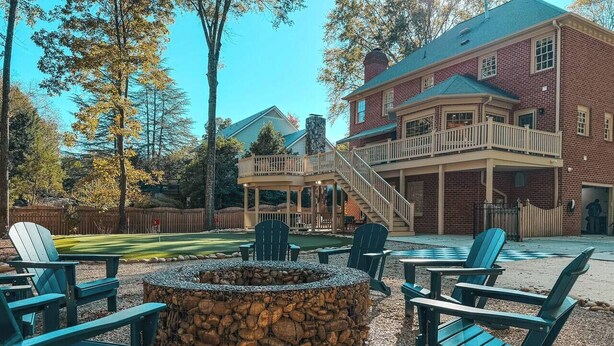 A stone fire pit surrounded by Adirondack chairs in a courtyard with a brick building in the background. - Putting Green - Life Sized Chess -Luxury Aesthetic (Greensboro)