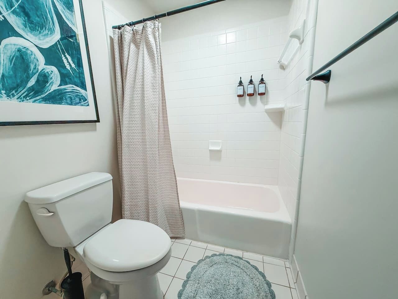 A bathroom with a toilet, a bathtub, a shower curtain, and a framed picture on the wall.