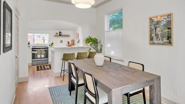 Eine moderne Küche mit weißen Schränken, einem eingebauten Backofen und einem Essbereich mit einem Holztisch und Stühlen.