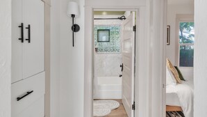 Ein Hotelzimmer mit einem weißen Kleiderschrank, einem Badezimmer mit einer Badewanne und einem Bett mit einem grünen Kopfkissen.
