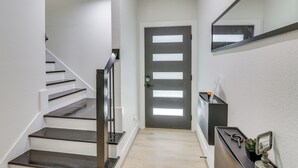 A modern hallway with a staircase, a dark door with horizontal panels, and a wall-mounted mirror. - East Downtown Walkability! Modern Houston Townhome (Houston)