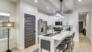 A modern kitchen with white cabinetry, a central island with bar stools, a refrigerator, and a pendant light. - East Downtown Walkability! Modern Houston Townhome (Houston)