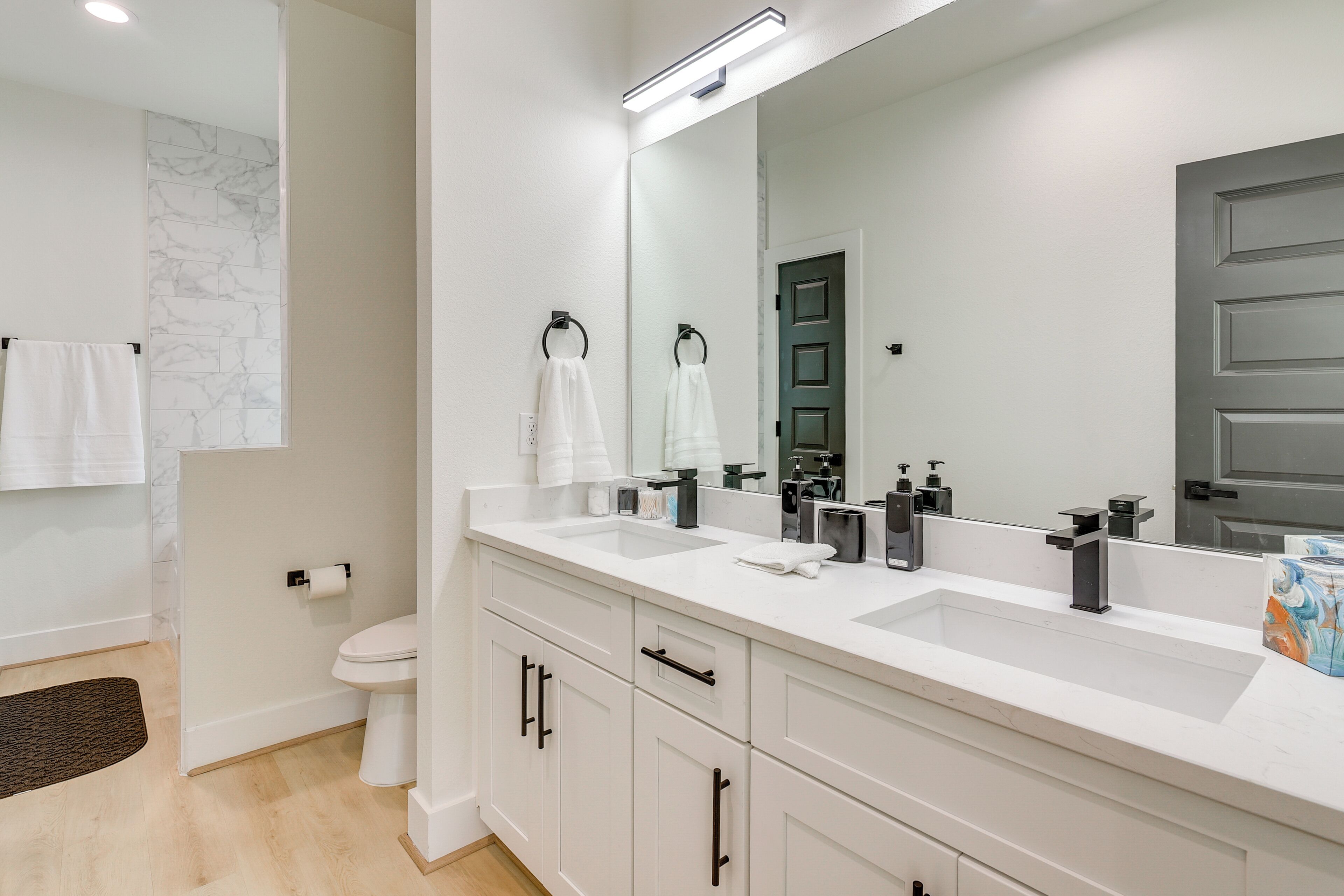 A modern bathroom with a white vanity, two sinks, a large mirror, and a toilet.