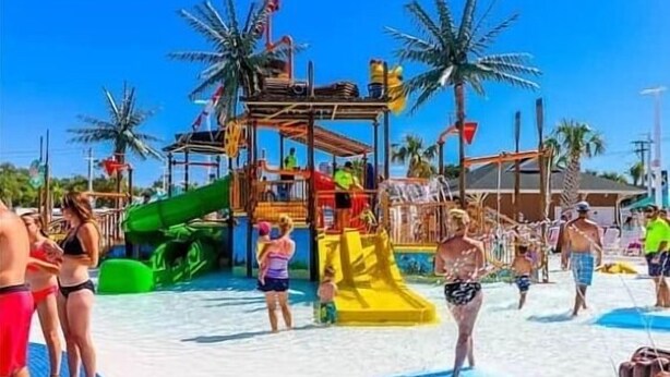 A water park with slides and play structures, surrounded by palm trees. - Surf Shack | Water Park | Ocean Lakes (Horry County)