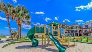 A beach playground with a slide, surrounded by palm trees and a beach. - Surf Shack | Water Park | Ocean Lakes (Horry County)