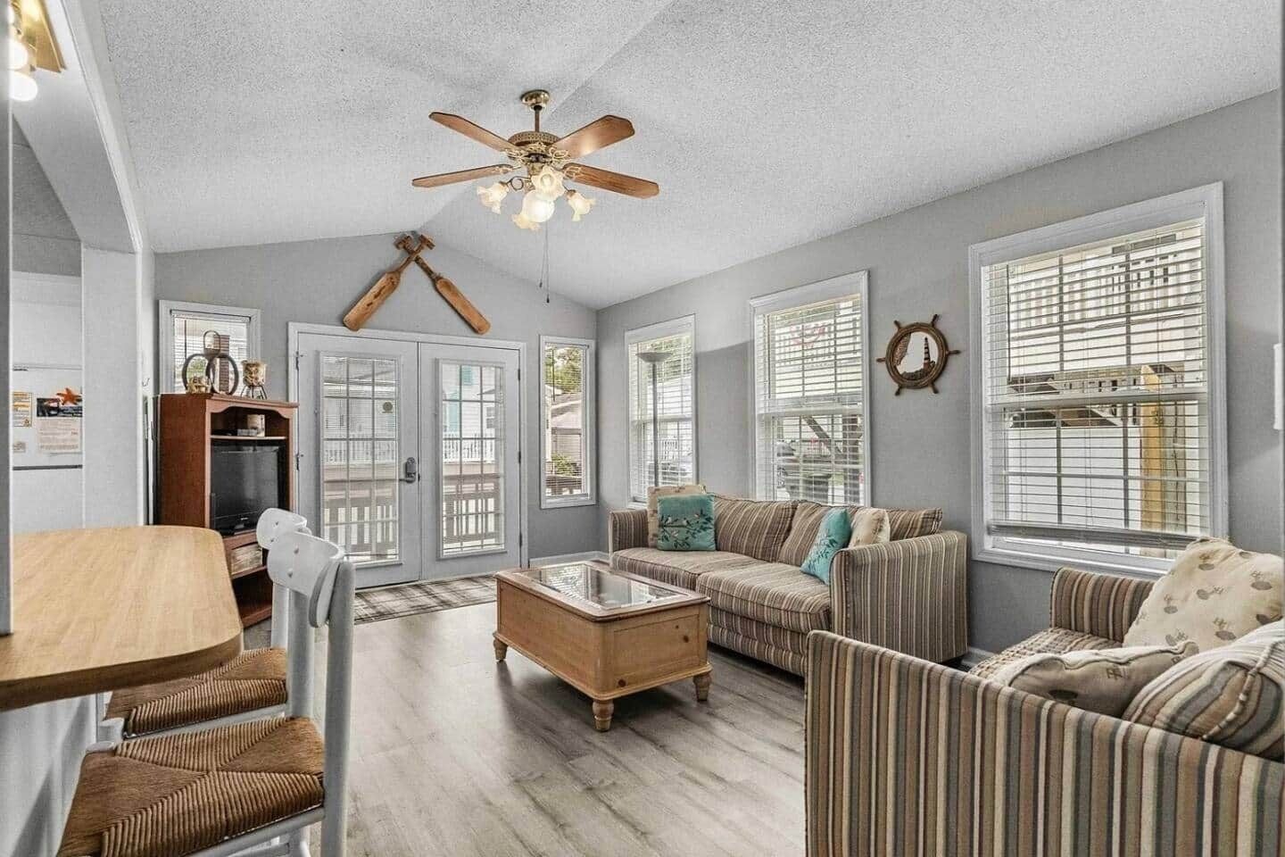 A spacious living room with a wooden coffee table, striped sofas, and a ceiling fan.