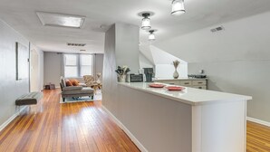 Eine moderne Küche mit weißem Arbeitsplatz, Holzboden und einem Essbereich mit einer Couch und Kissen.