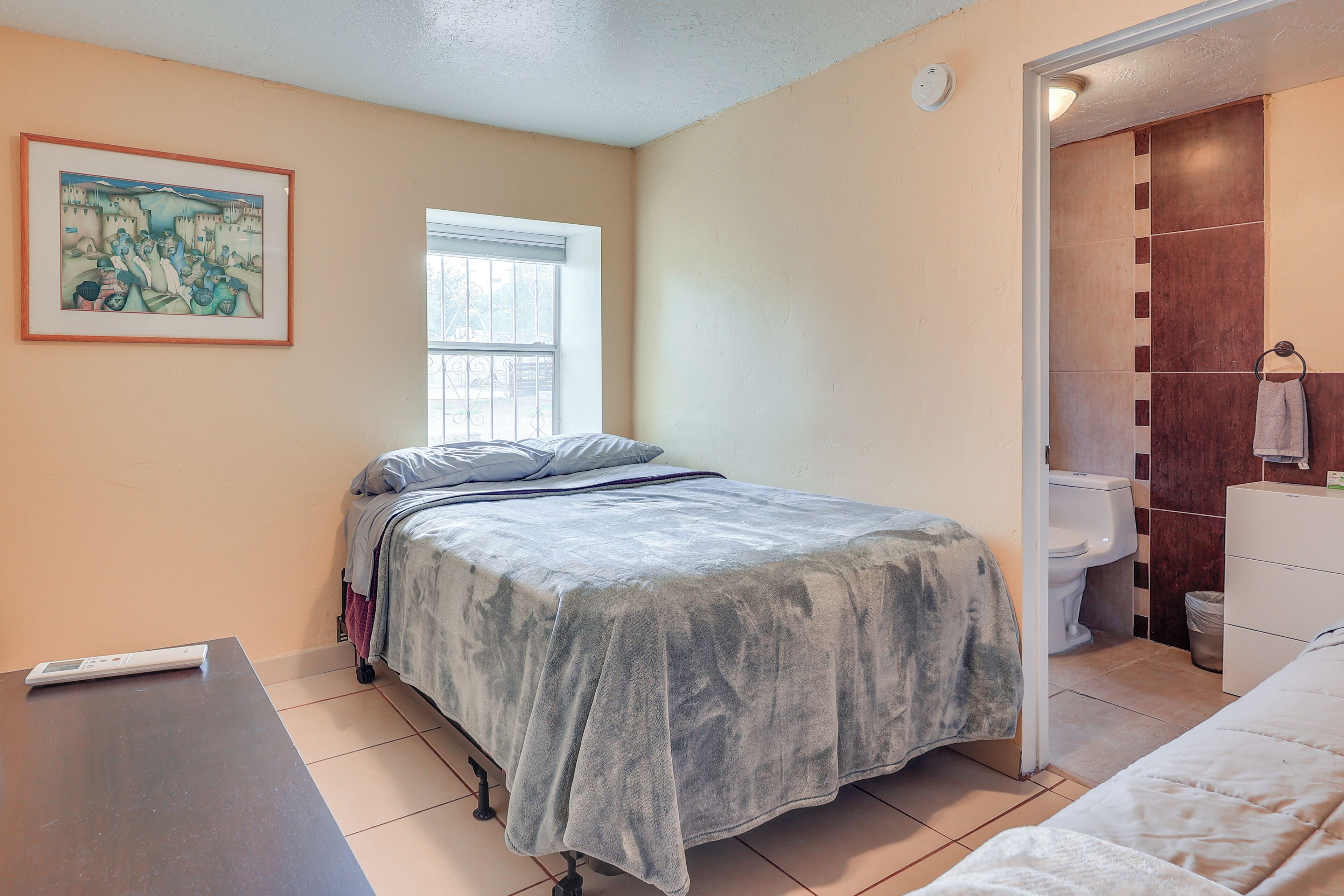 A bedroom with a bed, a window, a bedside table, and a bathroom visible through an open door.