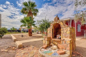 A stone structure with an arched entrance, surrounded by a gravel area with scattered bricks and a palm tree. - Walk Downtown: Authentic Adobe Home in Las Cruces! (Las Cruces)