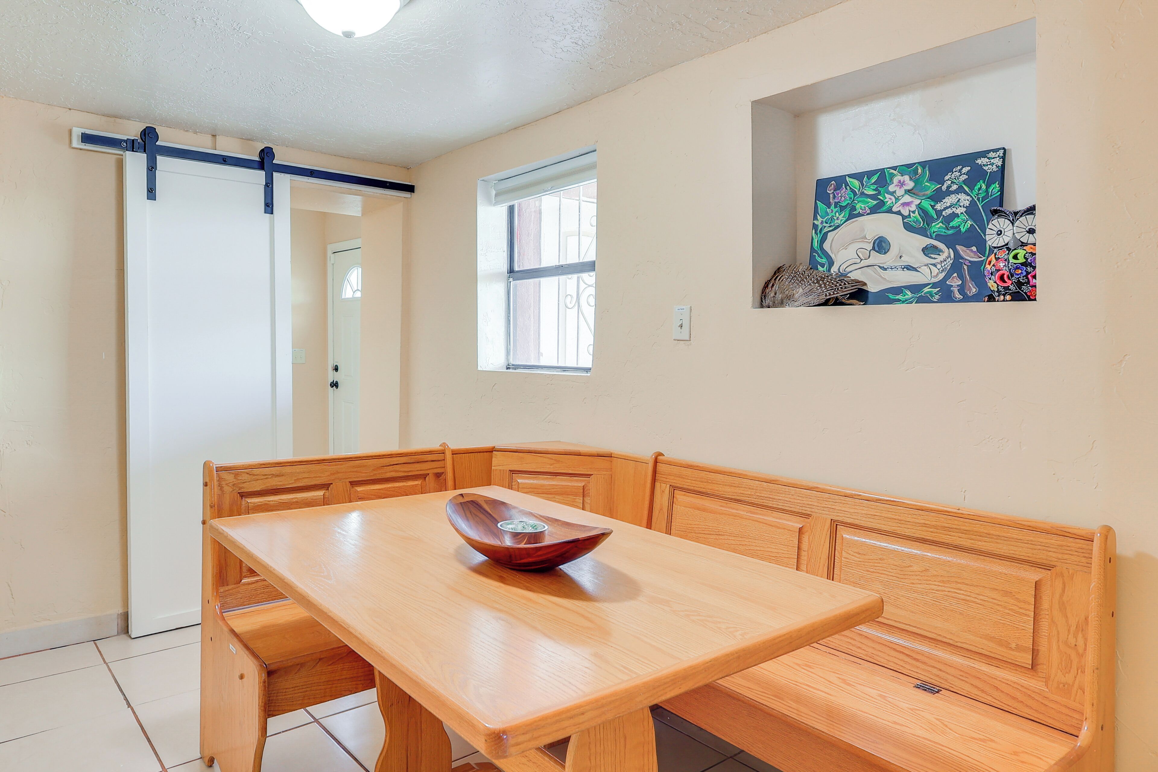 A dining area with a wooden table and bench, a small window, and a wall-mounted painting.