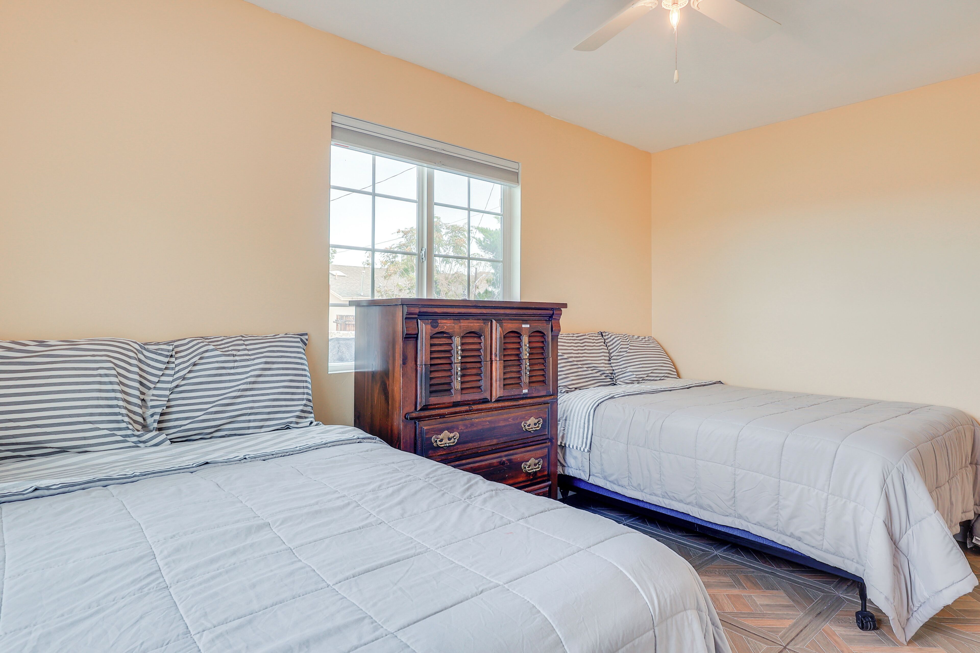 A bedroom with two beds, a dresser, and a window.