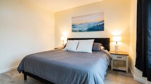 A bedroom with a bed, two bedside tables, a nightstand, and a painting on the wall.