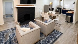A modern living room with a fireplace, two sofas, a dining area, and a kitchen. - 6-Bedroom 3-Bath Spacious Retreat 5 min to Downtown Indy Big Fenced-In Backyard (Indianapolis)