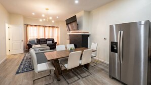 A modern living room with a dining area, a fireplace, and a large stainless steel refrigerator. - 6-Bedroom 3-Bath Spacious Retreat 5 min to Downtown Indy Big Fenced-In Backyard (Indianapolis)
