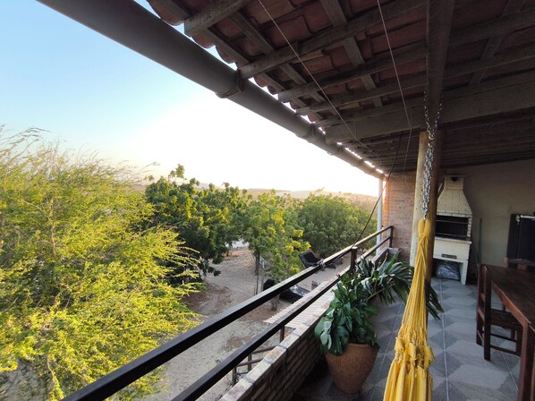 A balcony with a view of a lush green landscape, a hanging hammock, and a brick oven. - Jeri Suítes (2) Zona do Kite (Jijoca de Jericoacoara)