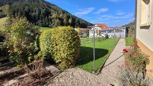 A residential area with a well-maintained lawn, a hedge, and a gravel path leading to a house with a red roof. - Cozy and stylish family-friendly vacation apartment in the middle of Simonswald (Simonswald)