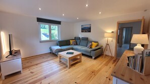 A modern living room with a sectional sofa, a coffee table, a lamp, and a bookshelf. - Cozy and stylish family-friendly vacation apartment in the middle of Simonswald (Simonswald)