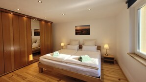 A bedroom with a large bed, wooden wardrobe, bedside lamps, and a window. - Cozy and stylish family-friendly vacation apartment in the middle of Simonswald (Simonswald)