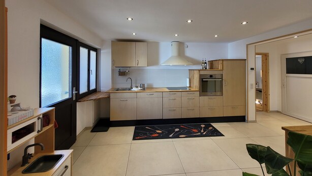 A modern kitchen with a central island, built-in oven, and a window with blinds. - Cozy and stylish family-friendly vacation apartment in the middle of Simonswald (Simonswald)