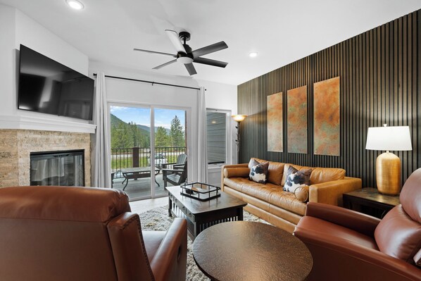A modern living room with leather furniture, a fireplace, a ceiling fan, and a large TV.