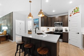 Une cuisine moderne dotée d’un îlot central, de tabourets de bar, de luminaires suspendus et d’un four à micro-ondes.