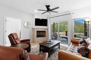 A living room with a fireplace, leather furniture, a ceiling fan, and a view of the outdoors.