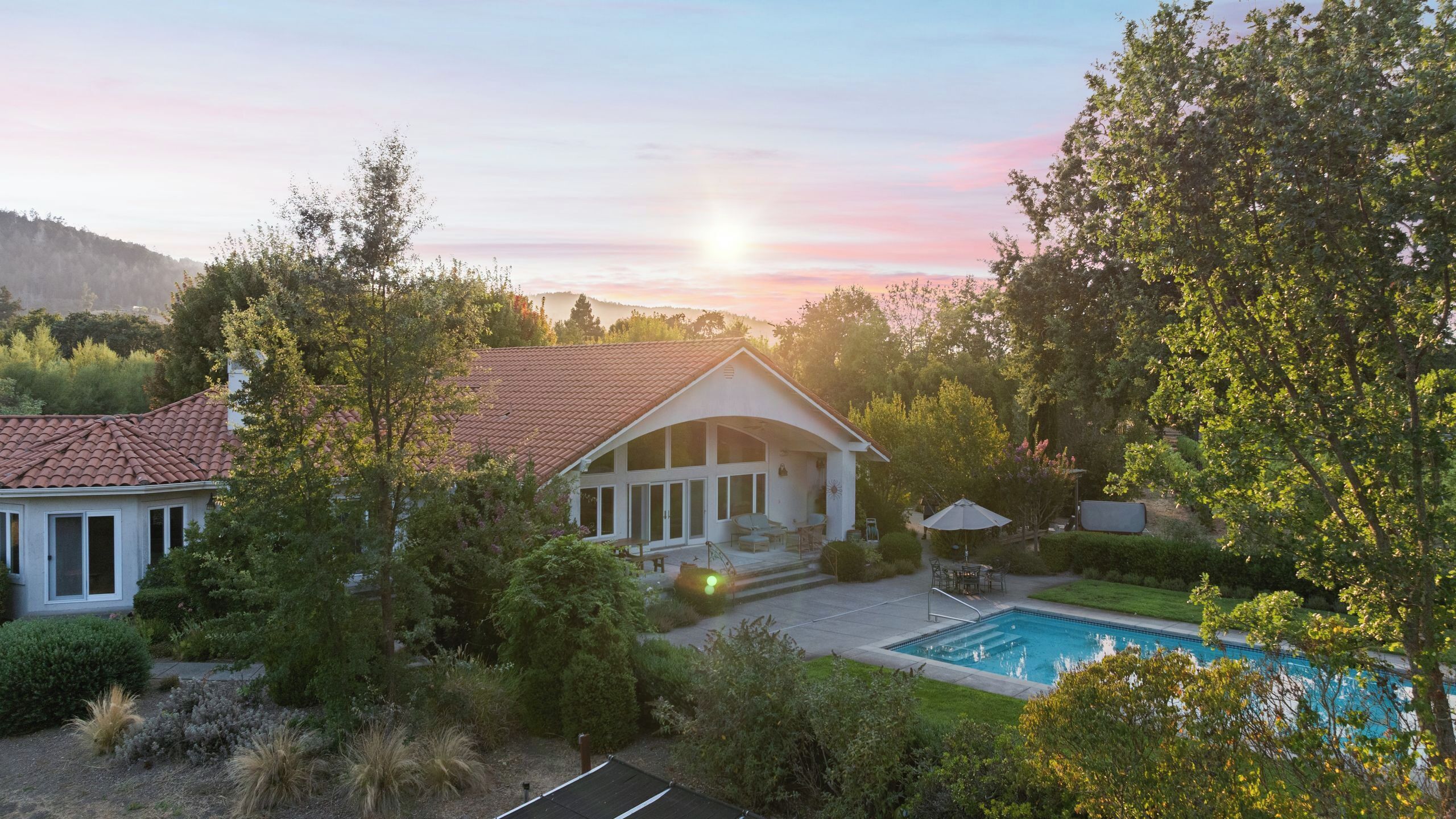 Ein Haus mit Schwimmbad, umgeben von Bäumen und einer hügeligen Landschaft.