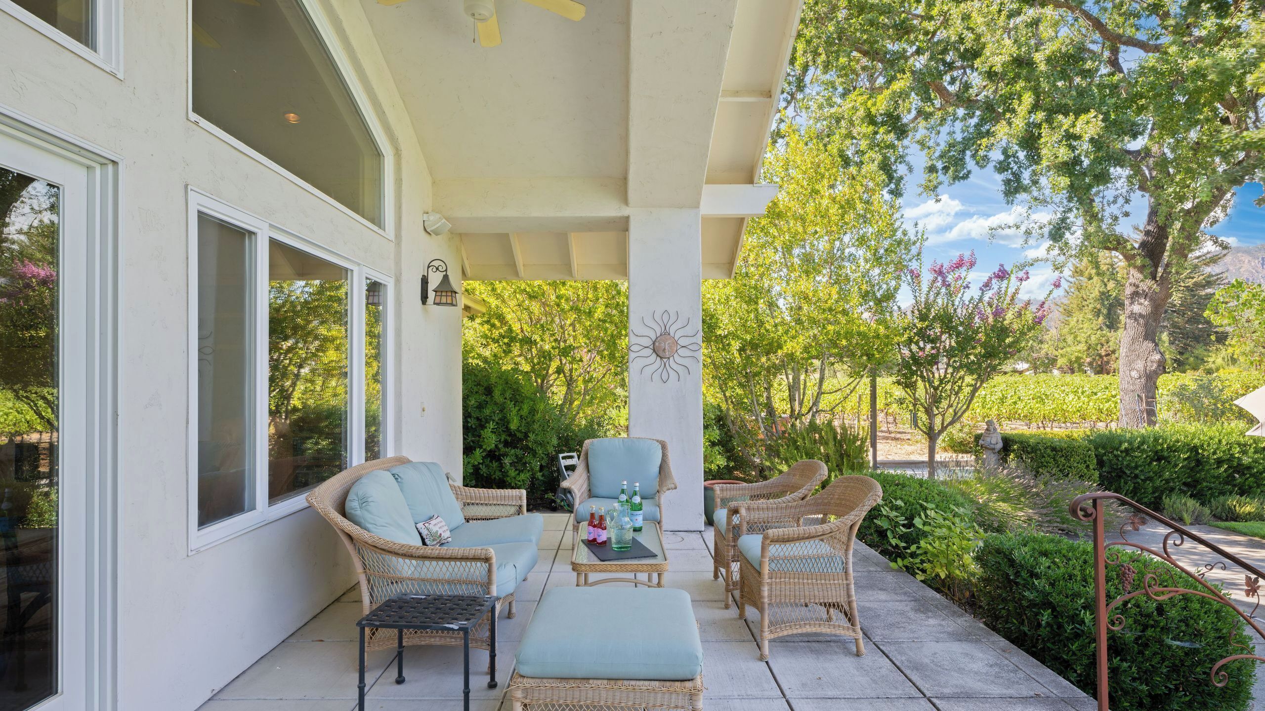 A covered patio with wicker furniture, a table with bottles, and a sun decoration.