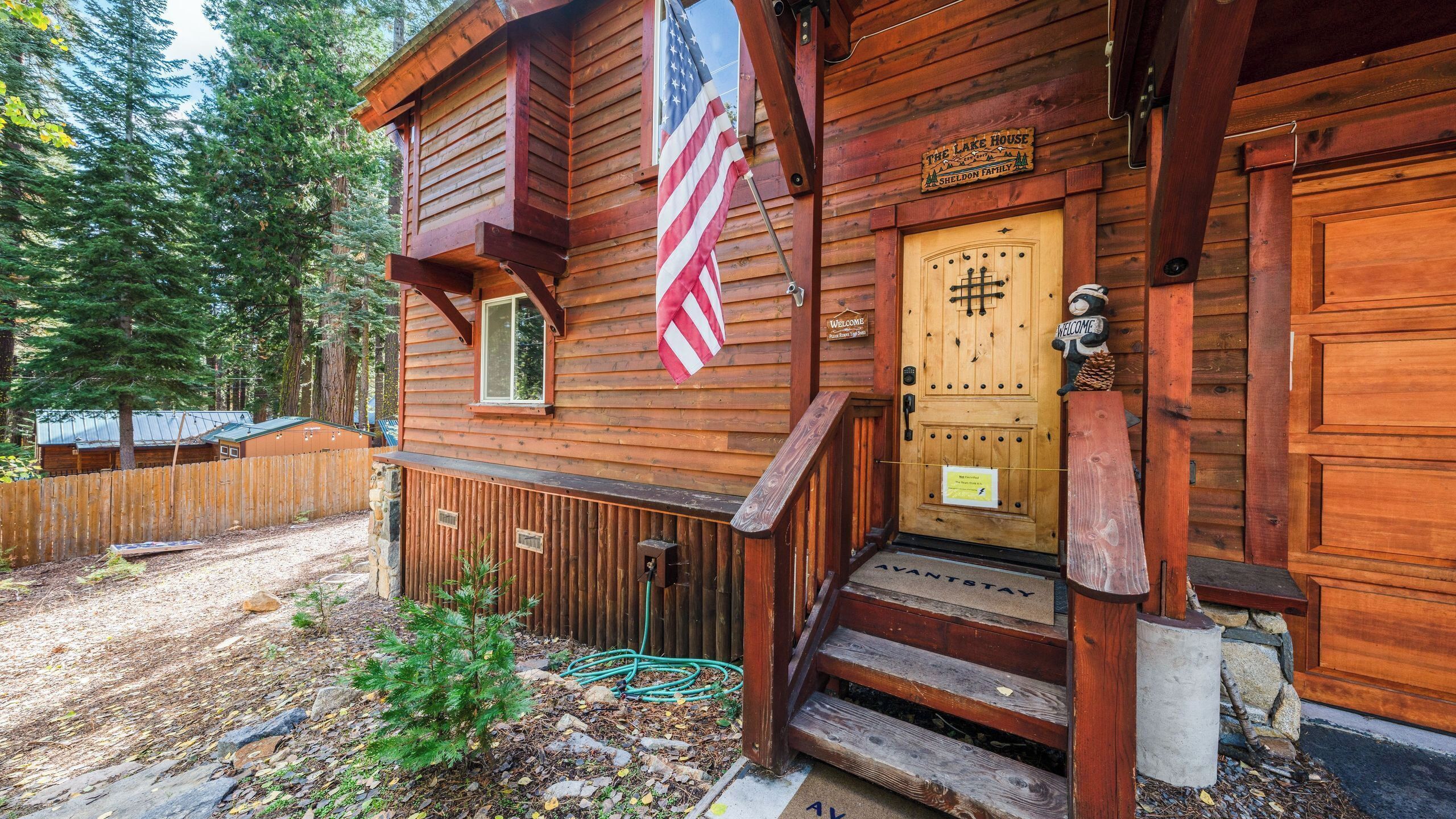 A wooden cabin with a wooden door, a welcome sign, and an American flag.